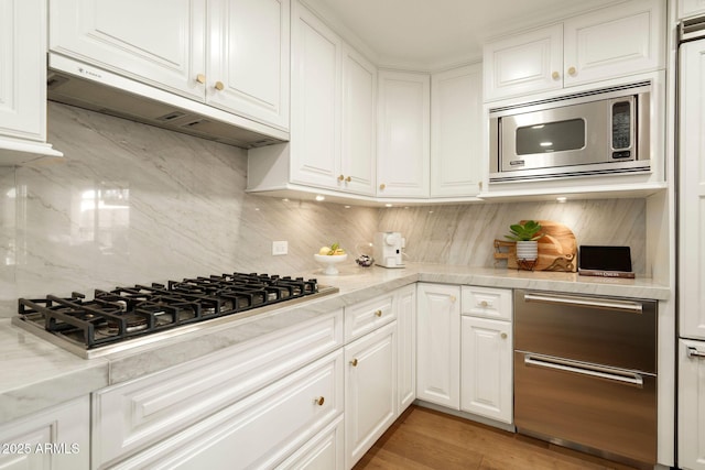 kitchen with stainless steel appliances, backsplash, white cabinets, and under cabinet range hood