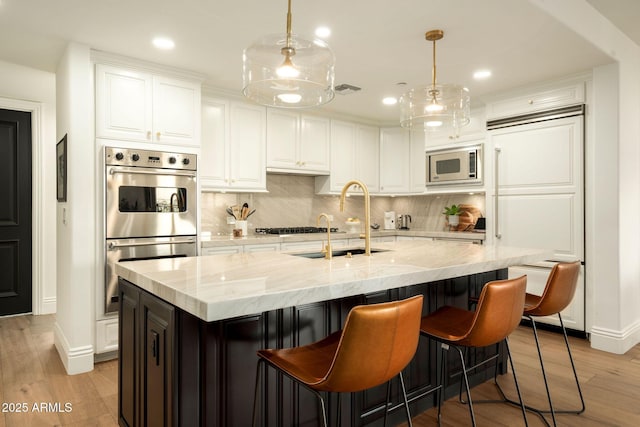 kitchen featuring light wood finished floors, tasteful backsplash, white cabinets, built in appliances, and a sink