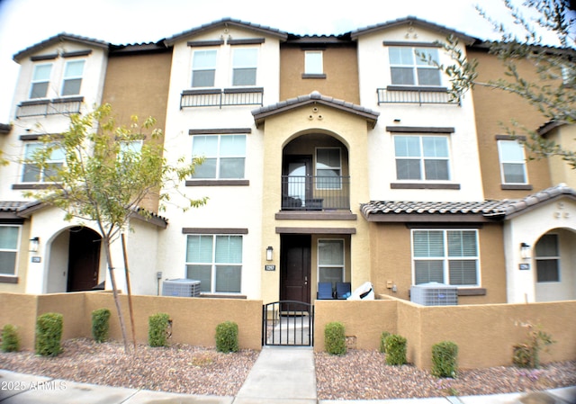 view of front of property featuring central AC unit, a fenced front yard, a tiled roof, a gate, and stucco siding