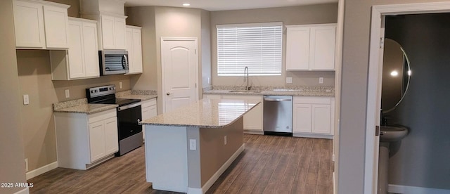 kitchen featuring stainless steel appliances, a sink, a kitchen island, white cabinetry, and light stone countertops