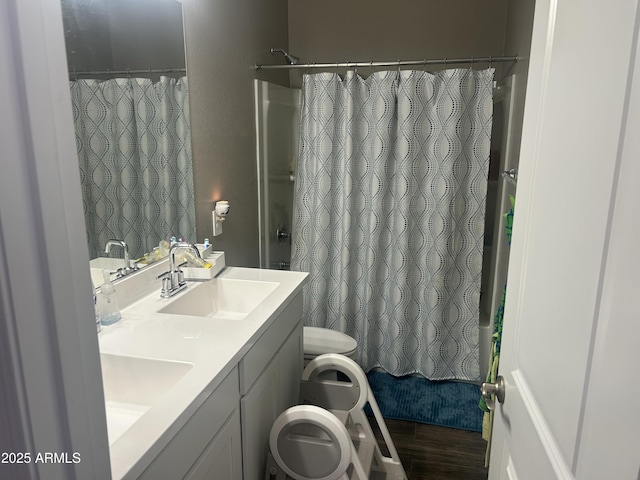 full bathroom featuring toilet, double vanity, a sink, and wood finished floors