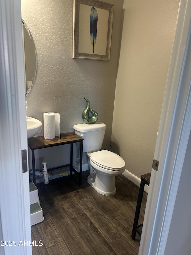 half bathroom featuring a textured wall, toilet, a sink, wood finished floors, and baseboards