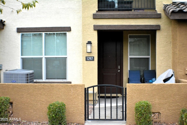 view of exterior entry featuring central AC, a gate, and stucco siding