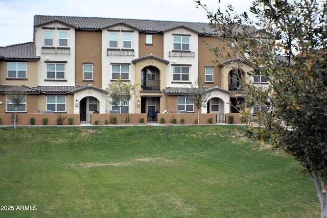 view of property featuring a tile roof, a front lawn, and stucco siding