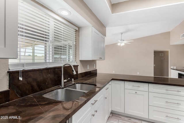 kitchen with ceiling fan, vaulted ceiling, dark stone countertops, white cabinets, and a sink