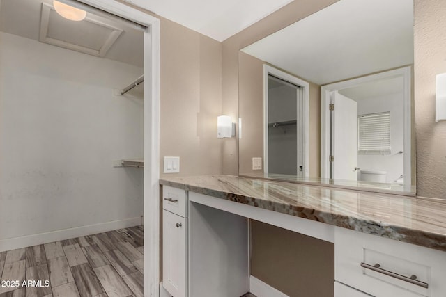 bathroom with a spacious closet, vanity, baseboards, and wood finished floors