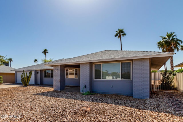 ranch-style home with fence, driveway, an attached garage, a shingled roof, and brick siding