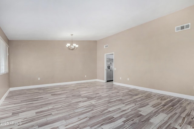 spare room with a chandelier, visible vents, light wood-type flooring, and baseboards