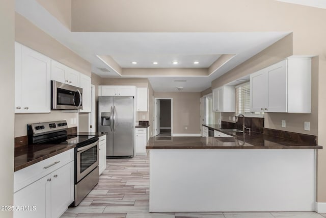 kitchen featuring a sink, dark countertops, appliances with stainless steel finishes, a peninsula, and a raised ceiling