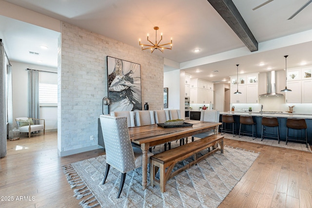 dining space with brick wall, light wood-type flooring, beam ceiling, and a notable chandelier