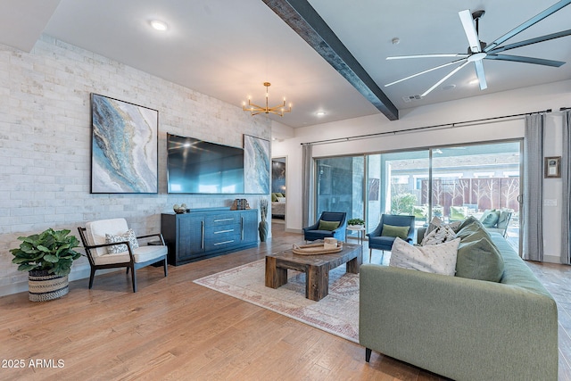 living area with ceiling fan with notable chandelier, visible vents, wood finished floors, and beamed ceiling