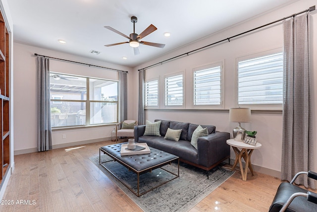 living room featuring light wood-type flooring, ceiling fan, visible vents, and baseboards