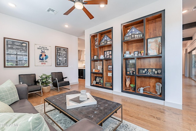 living room with ceiling fan, built in shelves, wood finished floors, visible vents, and baseboards