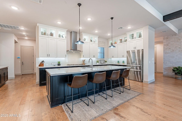 kitchen with visible vents, light countertops, appliances with stainless steel finishes, wall chimney exhaust hood, and an island with sink