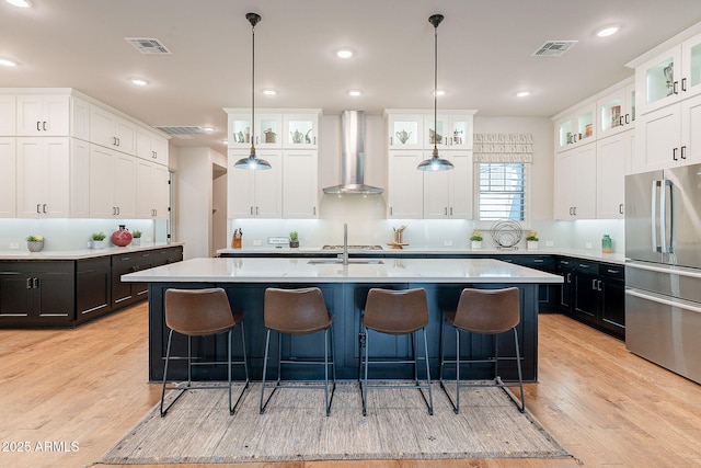 kitchen featuring wall chimney exhaust hood, light countertops, freestanding refrigerator, and white cabinetry