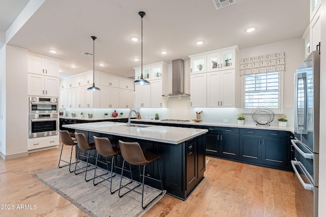 kitchen featuring a kitchen island with sink, stainless steel appliances, visible vents, wall chimney range hood, and a kitchen bar