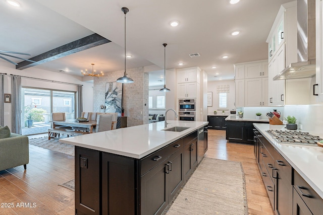 kitchen featuring light countertops, white cabinets, a sink, and wall chimney range hood