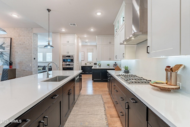 kitchen with stainless steel appliances, visible vents, white cabinetry, a sink, and wall chimney exhaust hood