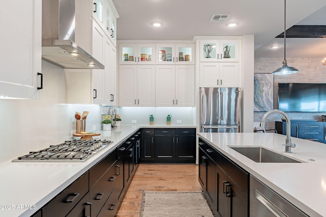 kitchen featuring a sink, visible vents, white cabinets, appliances with stainless steel finishes, and wall chimney exhaust hood