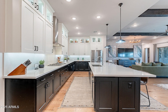 kitchen with a sink, white cabinets, light countertops, wall chimney range hood, and appliances with stainless steel finishes