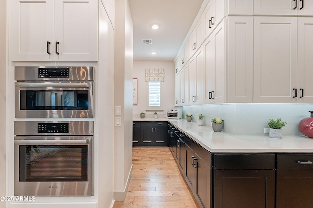 kitchen with light countertops, visible vents, double oven, white cabinetry, and light wood-type flooring