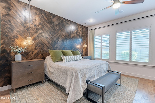 bedroom with an accent wall, a ceiling fan, wooden walls, light wood-type flooring, and baseboards