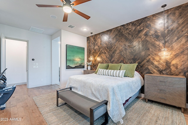 bedroom with baseboards, an accent wall, visible vents, and light wood-style floors