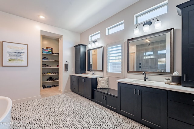 bathroom featuring baseboards, two vanities, a sink, and tiled shower