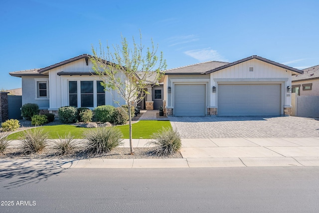 view of front of property featuring a garage, stone siding, decorative driveway, and a front yard