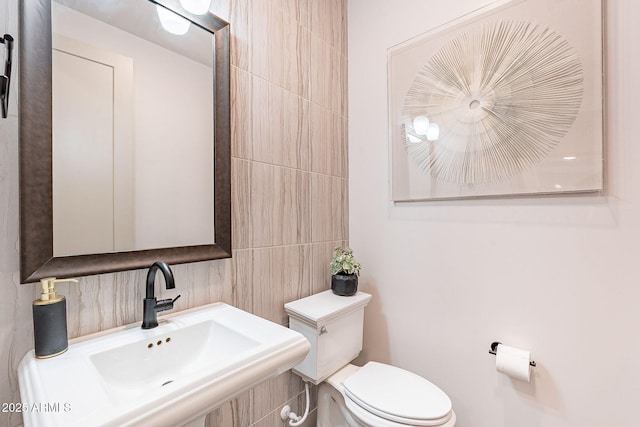 bathroom featuring a sink, toilet, and tile walls