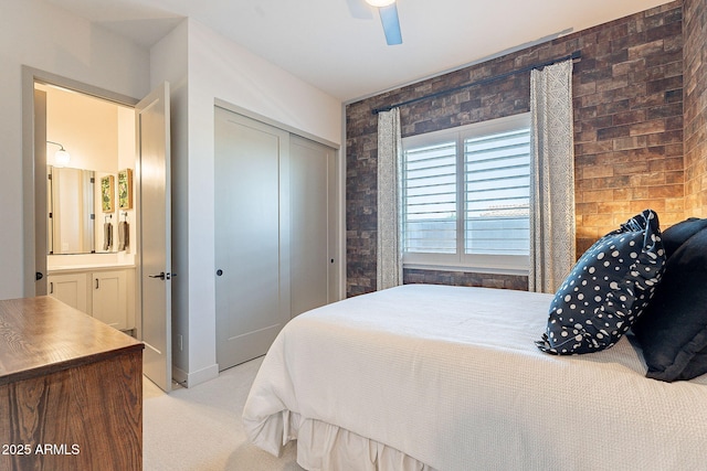 bedroom featuring light colored carpet, ceiling fan, brick wall, ensuite bathroom, and a closet