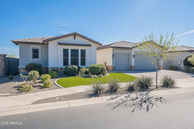 view of front facade with a garage, driveway, stone siding, a tiled roof, and a front lawn