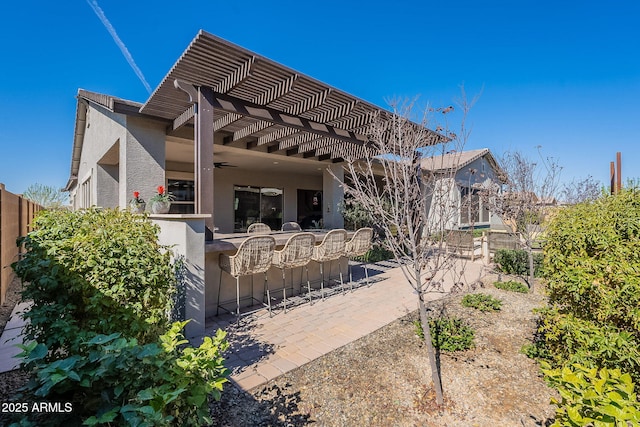 rear view of house with a patio, outdoor dry bar, fence, a pergola, and stucco siding