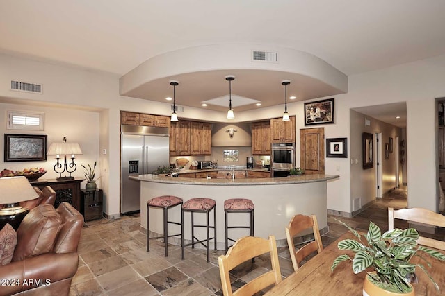 kitchen with stone countertops, hanging light fixtures, appliances with stainless steel finishes, and a breakfast bar area