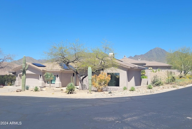 view of front of property featuring an attached garage, a mountain view, roof mounted solar panels, and stucco siding