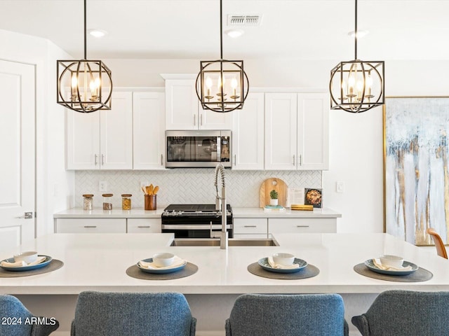 kitchen featuring a center island with sink, stainless steel appliances, white cabinets, and hanging light fixtures