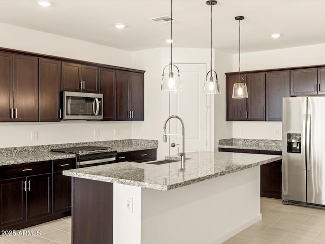 kitchen with appliances with stainless steel finishes, a kitchen island with sink, light stone countertops, pendant lighting, and sink