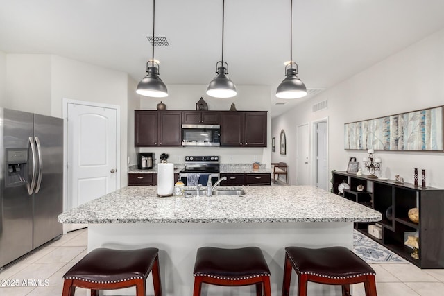 kitchen featuring appliances with stainless steel finishes, an island with sink, light tile patterned floors, dark brown cabinetry, and sink