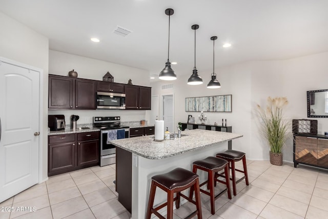 kitchen with a center island with sink, stainless steel appliances, light stone countertops, a kitchen bar, and dark brown cabinets