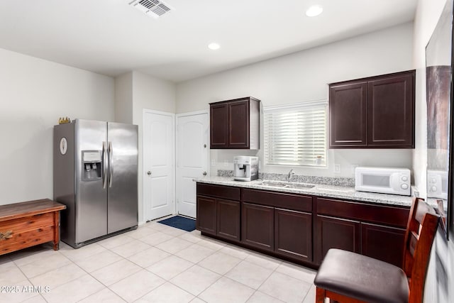 kitchen with sink, stainless steel fridge, dark brown cabinets, and light stone counters