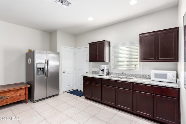 kitchen featuring stainless steel fridge with ice dispenser, light tile patterned floors, light stone counters, dark brown cabinetry, and sink