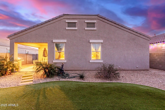 back house at dusk featuring a lawn and a patio area