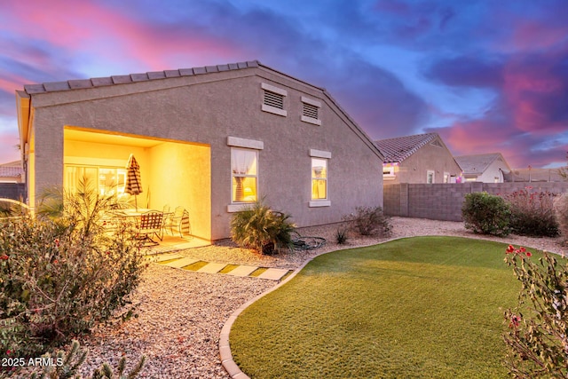 back house at dusk featuring a patio area and a yard