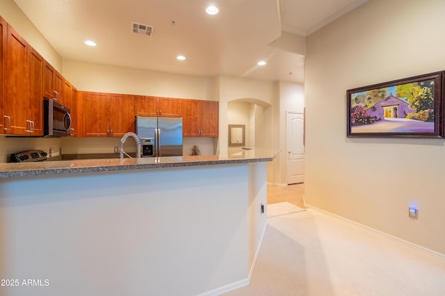 kitchen with visible vents, brown cabinetry, arched walkways, a peninsula, and stainless steel appliances