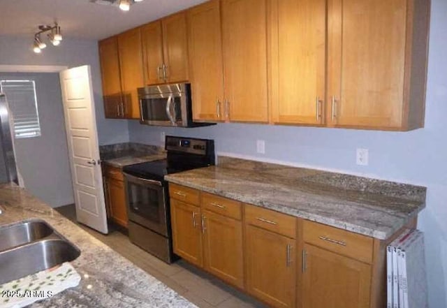 kitchen with light tile patterned floors, radiator heating unit, light stone countertops, stainless steel appliances, and a sink