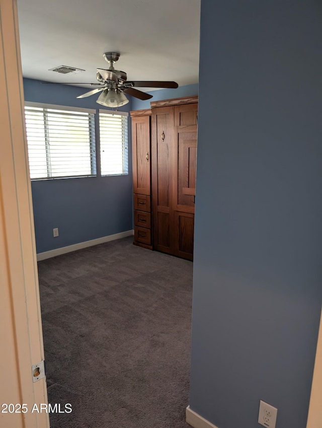 spare room with baseboards, visible vents, dark colored carpet, and a ceiling fan