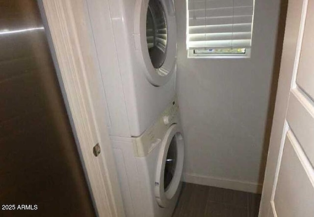 laundry area with laundry area, baseboards, and stacked washer / dryer