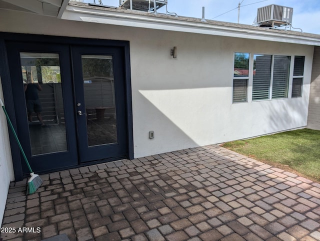 entrance to property with cooling unit, french doors, a patio, and stucco siding