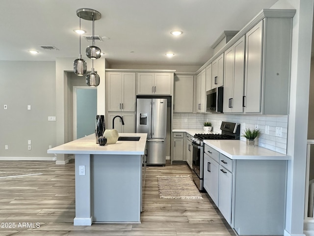 kitchen featuring light hardwood / wood-style flooring, appliances with stainless steel finishes, sink, decorative light fixtures, and tasteful backsplash