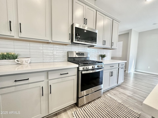 kitchen with light hardwood / wood-style floors, backsplash, and appliances with stainless steel finishes